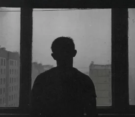 black and white photo of man standing in front of a window