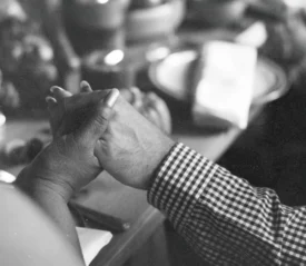 Two people hold hands across a table set with plates, bowls, and candles in a warm, intimate setting