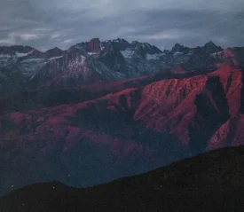 Mountain range at sunset with rugged peaks and slopes glowing red under dramatic clouds