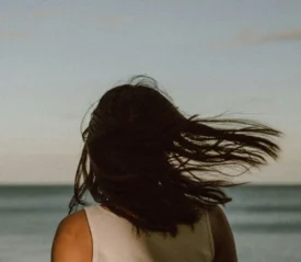 girls hair blowing in the wind as she stands in front of the ocean