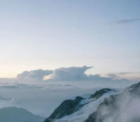 A serene mountain landscape with snowy peaks and clouds stretching across the horizon at sunrise or sunset