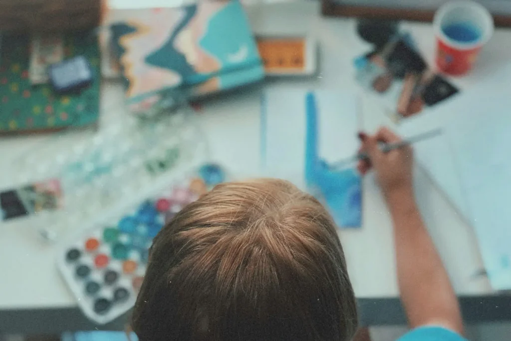 Overhead view of a person painting with watercolors at a cluttered art desk
