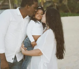 father and mother kissing their child