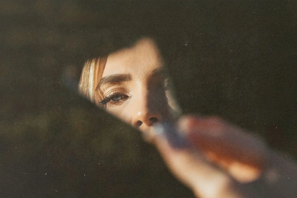 A hand holds a piece of cracked mirror with warm light illuminating the fingers