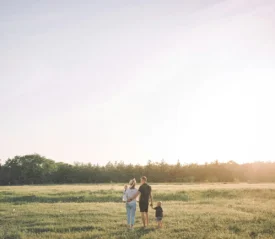 A family walking together through an open grassy field at sunset, holding hands and enjoying the warm light