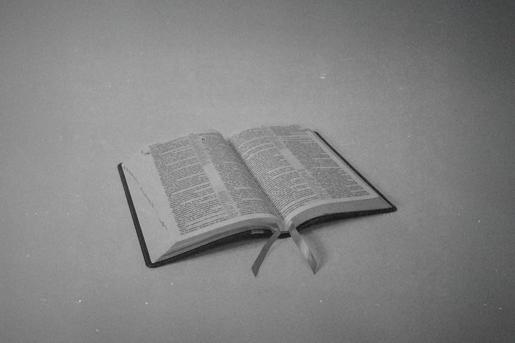 Black‑and‑white image of an open Bible resting on a flat surface with two ribbon bookmarks