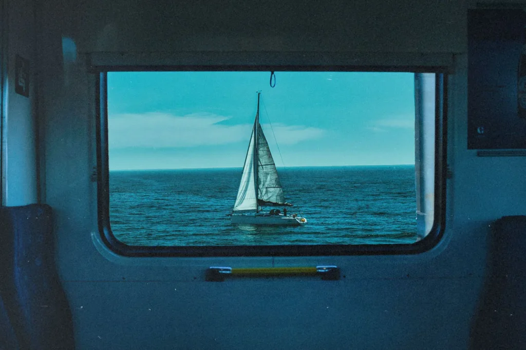 Sailboat on a calm blue ocean framed perfectly within a train window, with clear sky above the horizon