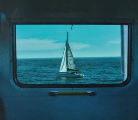 Sailboat on a calm blue ocean framed perfectly within a train window, with clear sky above the horizon