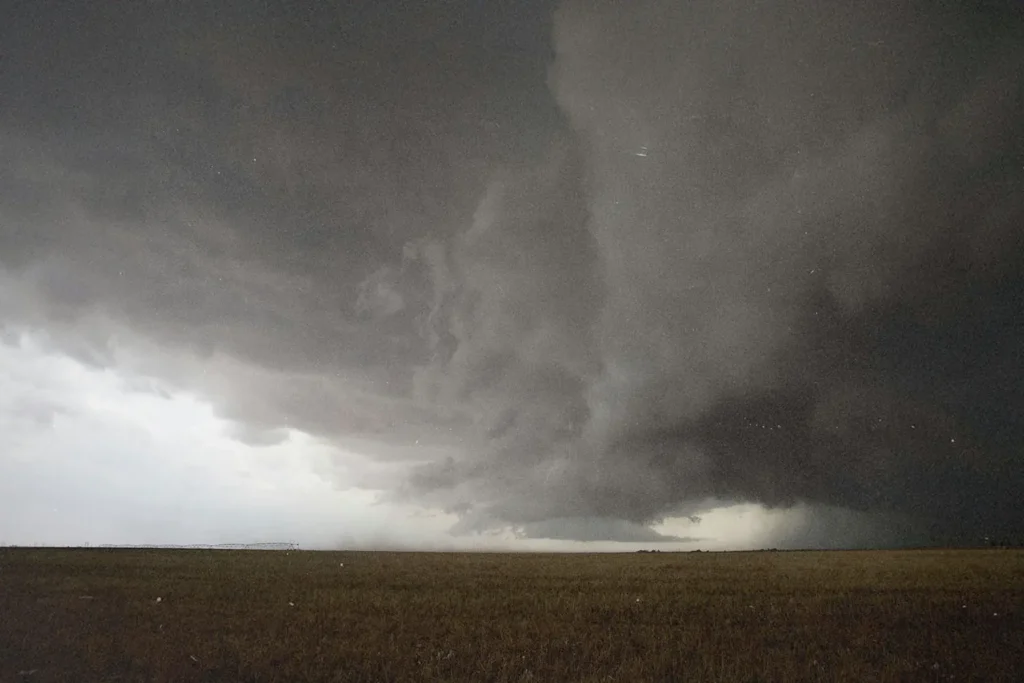 Massive storm cloud spreads dramatically across the sky above a flat, open field