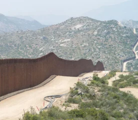 Long winding security wall running through a rugged, mountainous landscape with dirt roads following its path