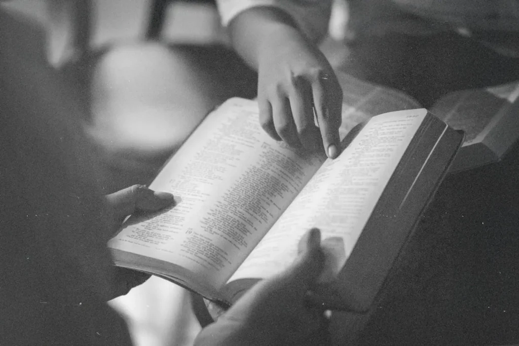 Two people read an open Bible together, one person pointing to a passage on the page