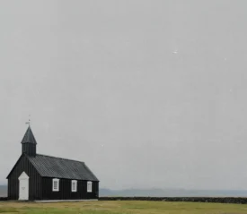 Rustic wooden church building in the distance of an open foggy field