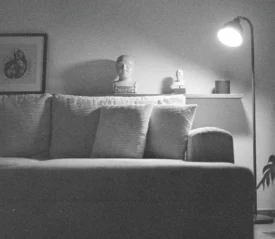 A cozy living room with a soft couch, a floor lamp casting warm light, framed art on the wall, and decorative objects arranged on a shelf