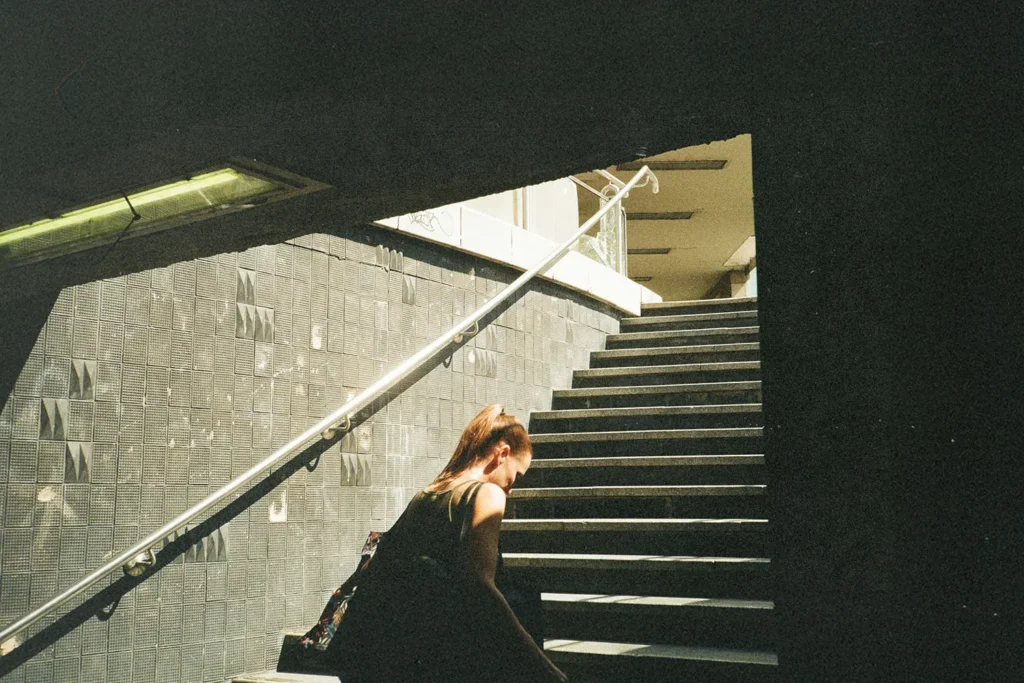 Person walking up a dimly lit stairway toward bright sunlight at the top of an urban underpass