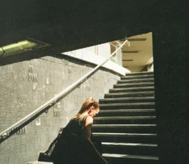 Person walking up a dimly lit stairway toward bright sunlight at the top of an urban underpass