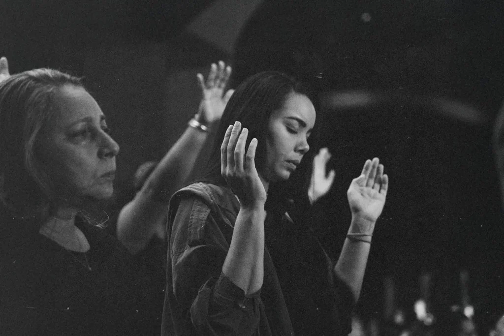 black and white photo of people with hands int he air praising