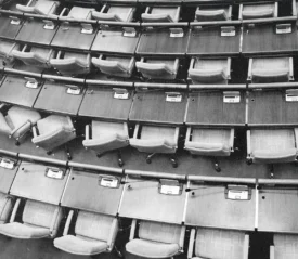 Rows of empty seats and wooden desks curve around an auditorium in a tiered arrangement