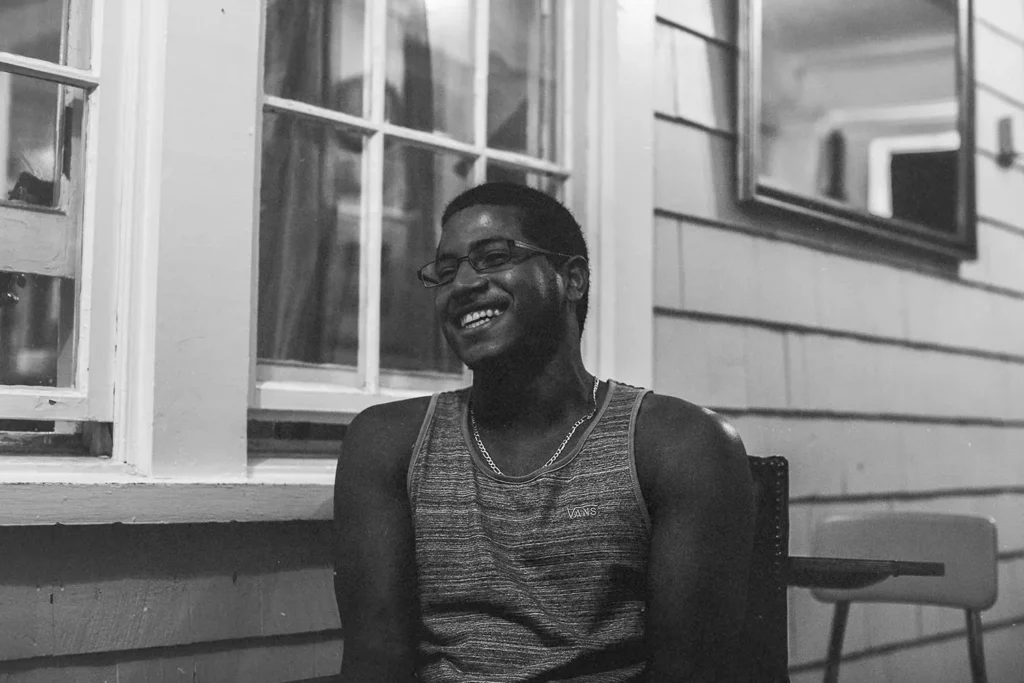 man laughing while sitting in a chair on a porch