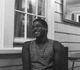 man laughing while sitting in a chair on a porch