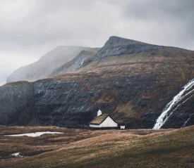 ll white church with a grass roof nestled in a vast mountain valley beside a cascading waterfall
