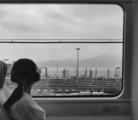 Girl with headphones on looking out a train window towards the city