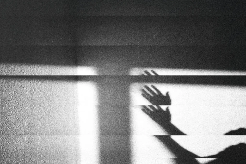 Shadow of raised hands cast across a textured wall in dramatic light and dark bands