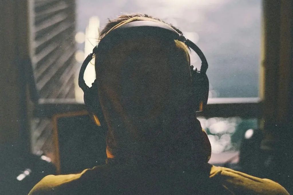 A person wearing large headphones is silhouetted against soft window light, with the background slightly out of focus