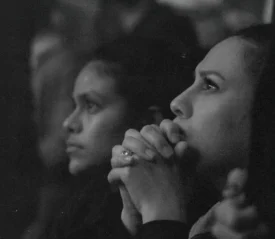 Two women looking focused towards the distance, one with hands folded on her chin