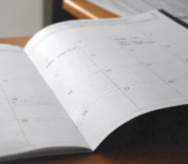 An open planner lies on a desk, showing a monthly calendar layout with faint handwritten notes
