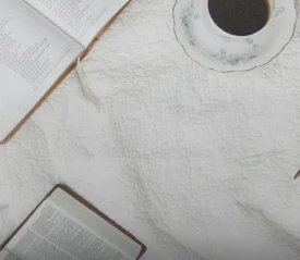 Two open books and a cup of coffee rest on a white quilted blanket