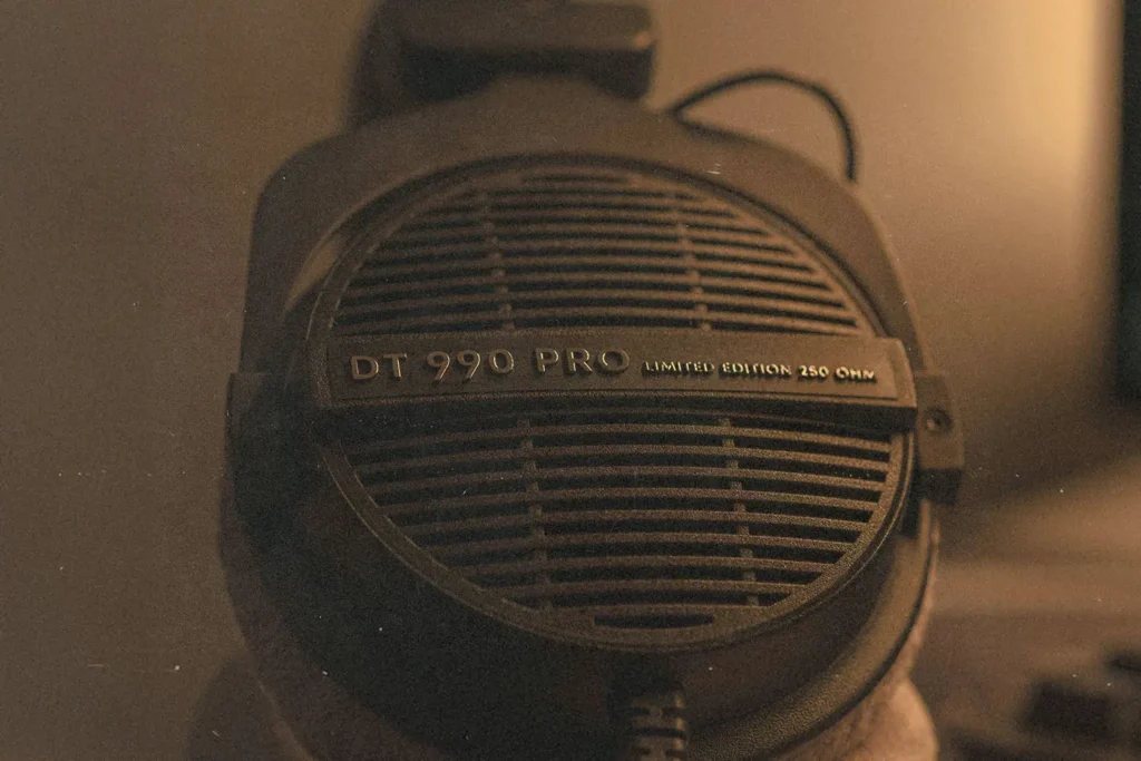A close-up of a pair of studio headphones labeled “DT 990 PRO,” lit in warm, low lighting