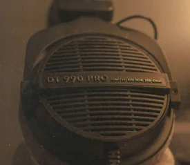 A close-up of a pair of studio headphones labeled “DT 990 PRO,” lit in warm, low lighting