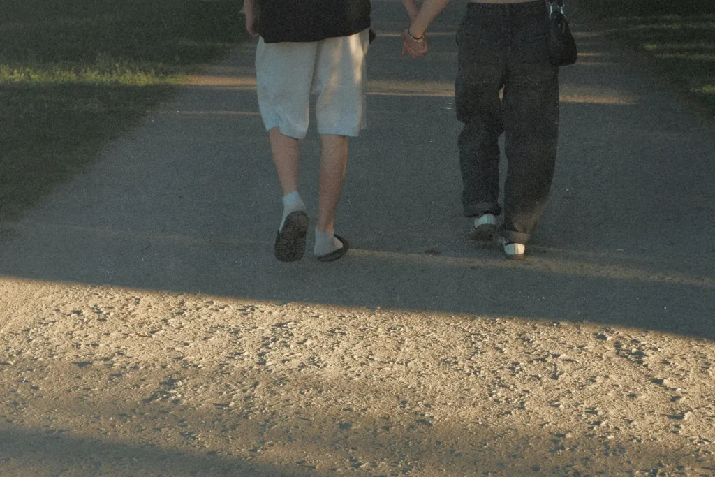 Two people walking hand in hand down a sunlit pathway in a park.