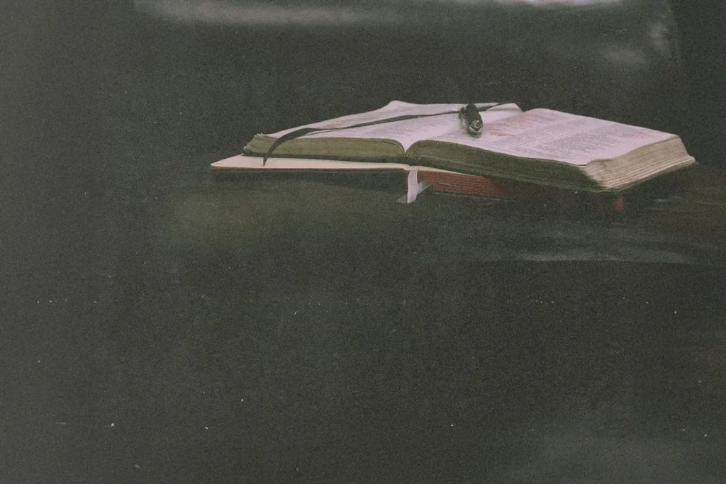 Open Bible resting on a dark leather surface with a ribbon marker and soft, moody lighting