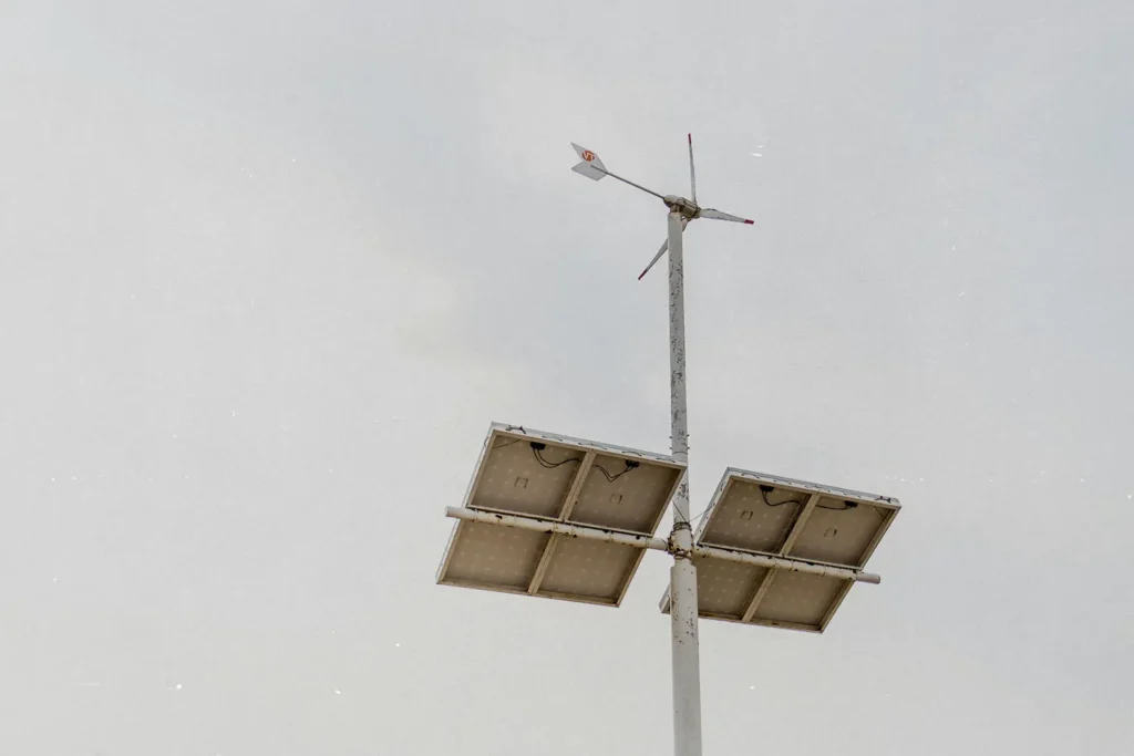 Solar panels mounted on a tall pole with a small wind turbine against a pale sky.
