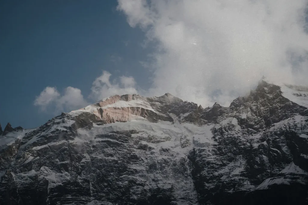 Snow on a rocky mountain with a cloudy blue sky in the background