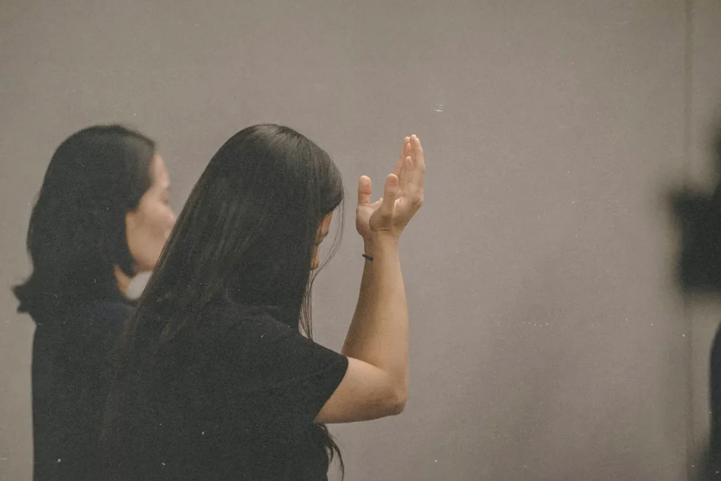 Woman wearing all black with head bowed and arms raised