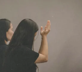 Woman wearing all black with head bowed and arms raised