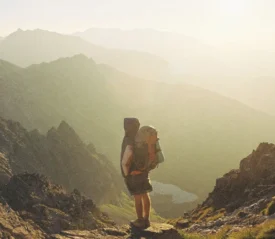 Man with camping gear looking out into the horizon with mountains in the background