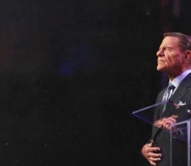 Kenneth Copeland praying at pulpit with black background