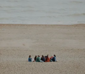 Group of people sitting in a circle in the sand with the ocean in the distance
