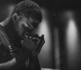 Man with head bowed and hands clasped to pray