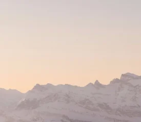 Snow-covered mountain range under a soft pastel sunrise sky