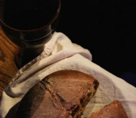 broken bread on a cloth napkin next to a communion cup on the edge of a wooden table
