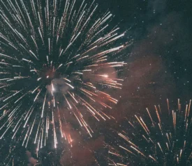 A night sky filled with large bursts of fireworks in bright white and orange tones