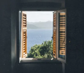 unlit seascape framed by an open window overlooking blue water and rolling hills