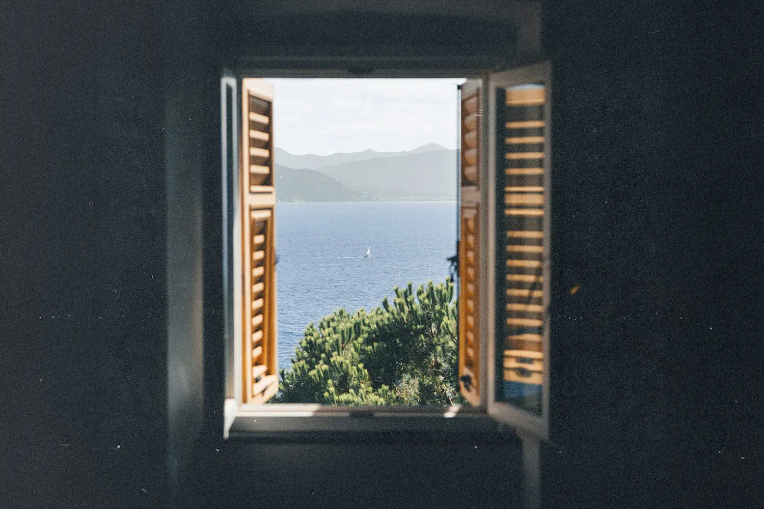 unlit seascape framed by an open window overlooking blue water and rolling hills