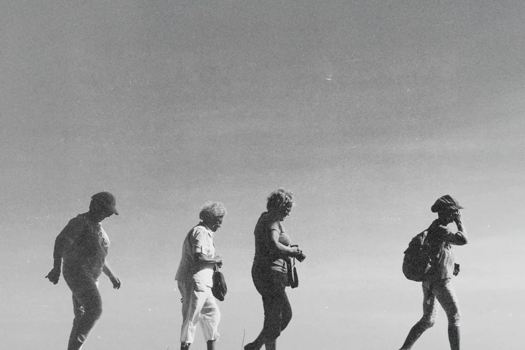 Four people walk in a line across an open landscape, silhouetted against a bright sky