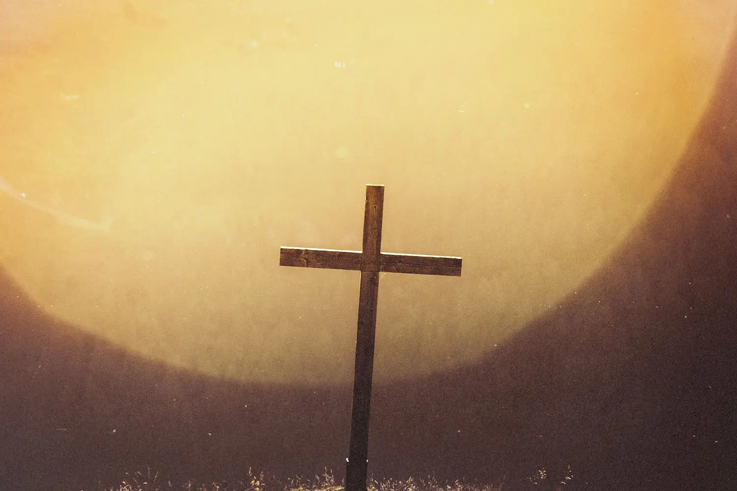 Wooden cross standing in front of a glowing golden light, creating a warm and reverent atmosphere
