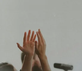 Two hands lifted upward in a gesture of worship or praise against a plain background